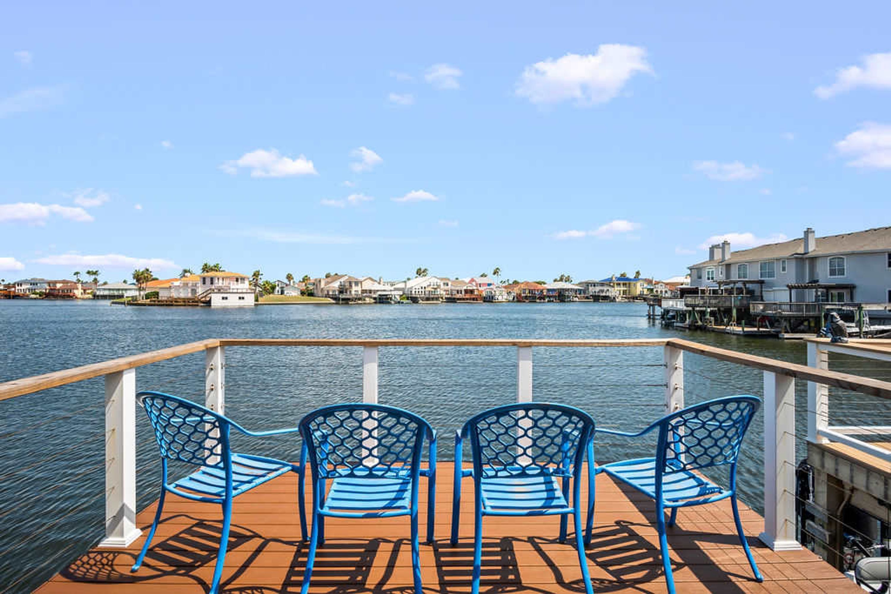 A waterfront deck with three blue chairs and a railing.