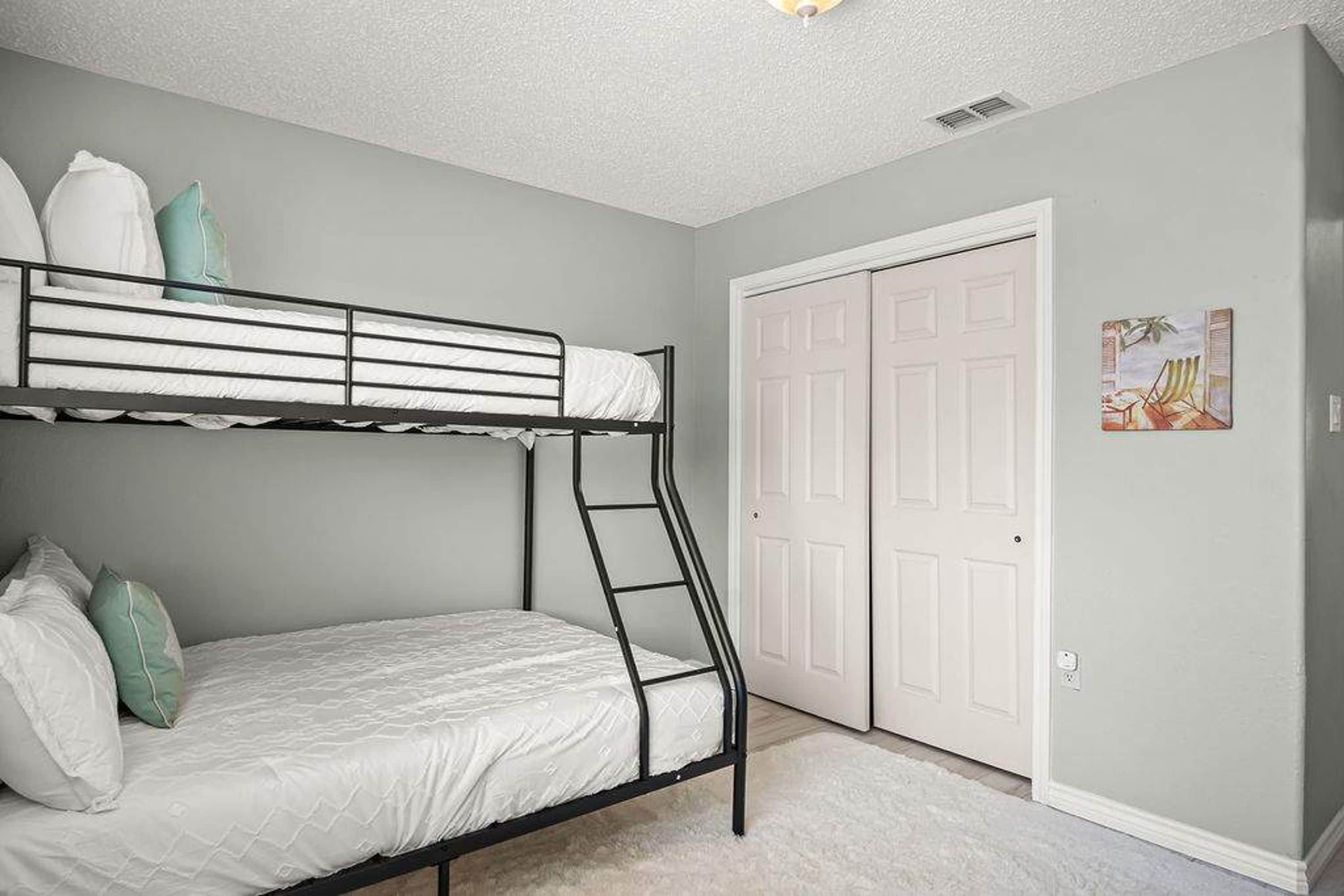 A bunk bed room with a ladder, white bedding, and a door with a picture on the wall.