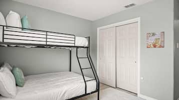 A bunk bed room with a ladder, white bedding, and a door with a picture on the wall.