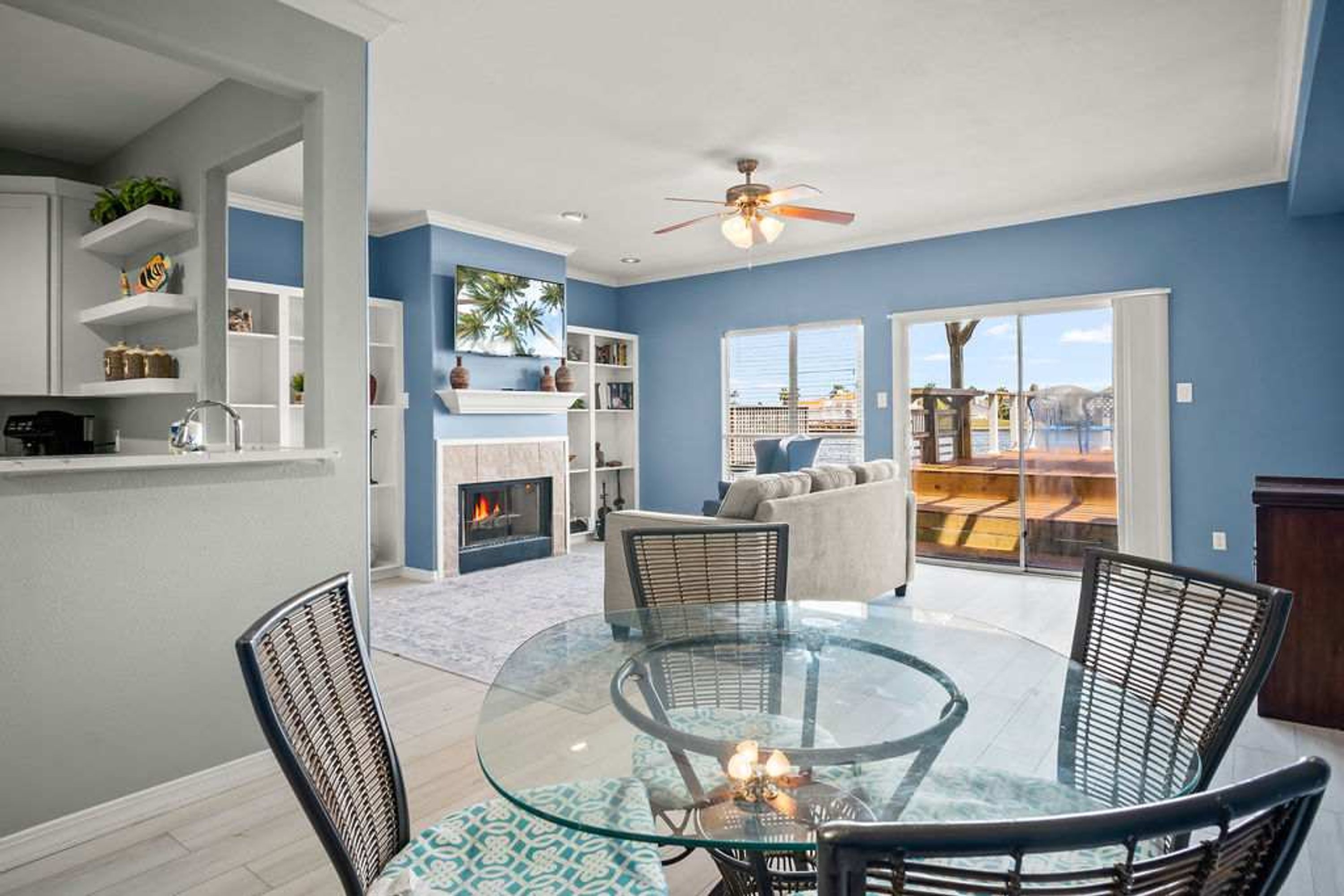 A modern living room with a glass-top table, wicker chairs, a fireplace, and a view of the outdoors.