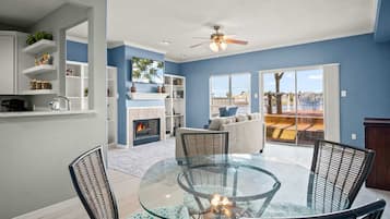 A modern living room with a glass-top table, wicker chairs, a fireplace, and a view of the outdoors.
