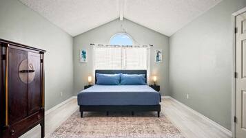 A bedroom with a bed, a nightstand, a dresser, and a window with curtains.
