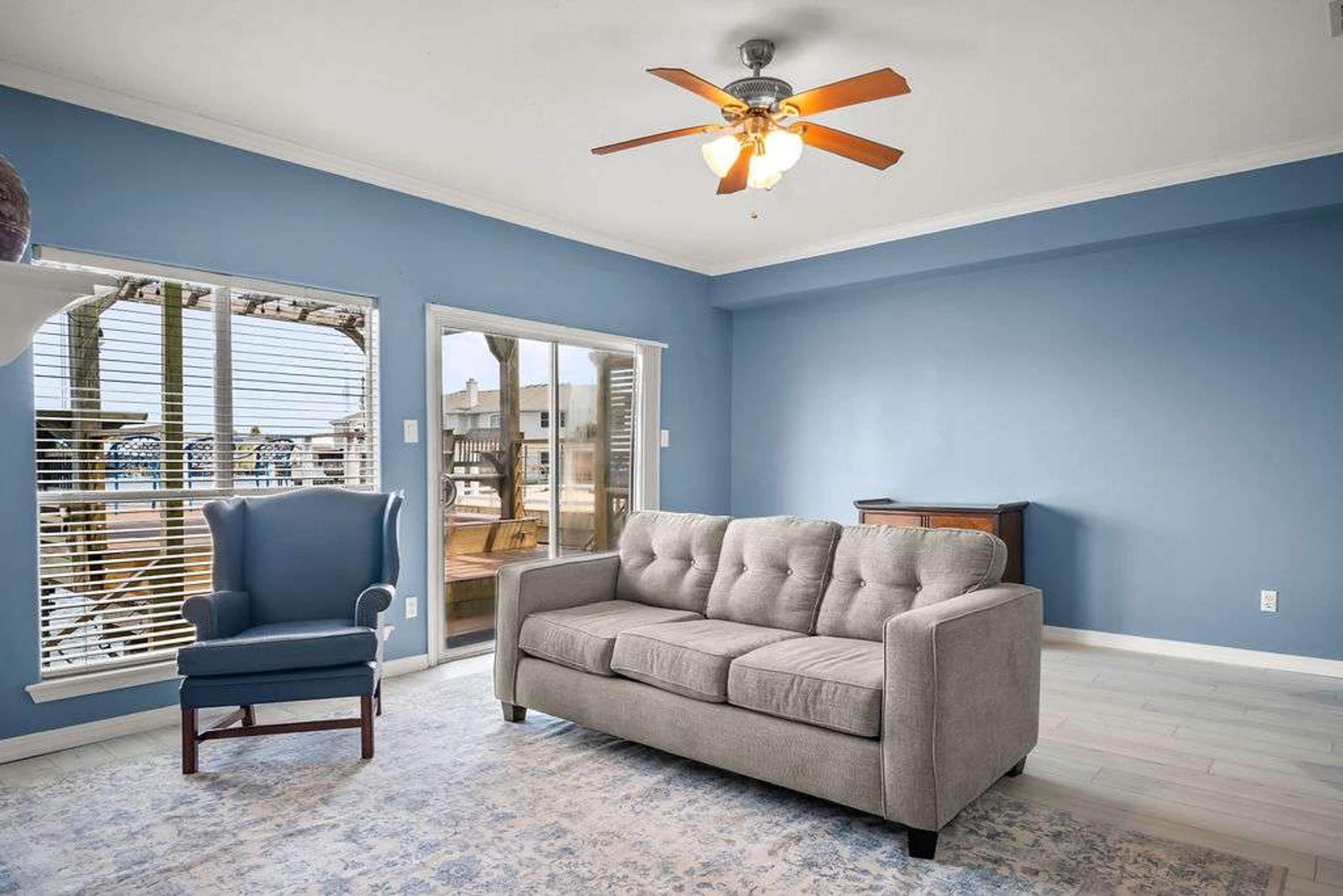A living room with a ceiling fan, a sofa, a chair, and a view through a glass door.