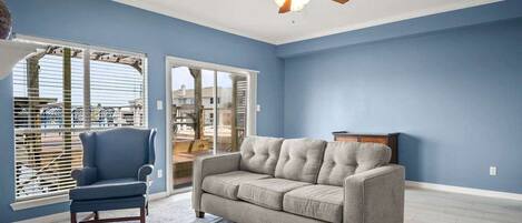 A living room with a ceiling fan, a sofa, a chair, and a view through a glass door.