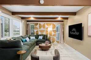 Ein Wohnzimmer mit Ecksofa, Couchtisch und Wandfernseher.