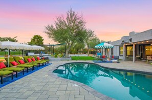 A swimming pool area with lounge chairs and umbrellas, surrounded by a landscaped garden and a building with outdoor seating. - Scottsdale Retreat Pool Pickleball Spa (Scottsdale)