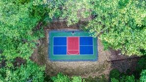 Eine Vogelperspektive auf einen Tennisplatz, umgeben von dichtem Grün.