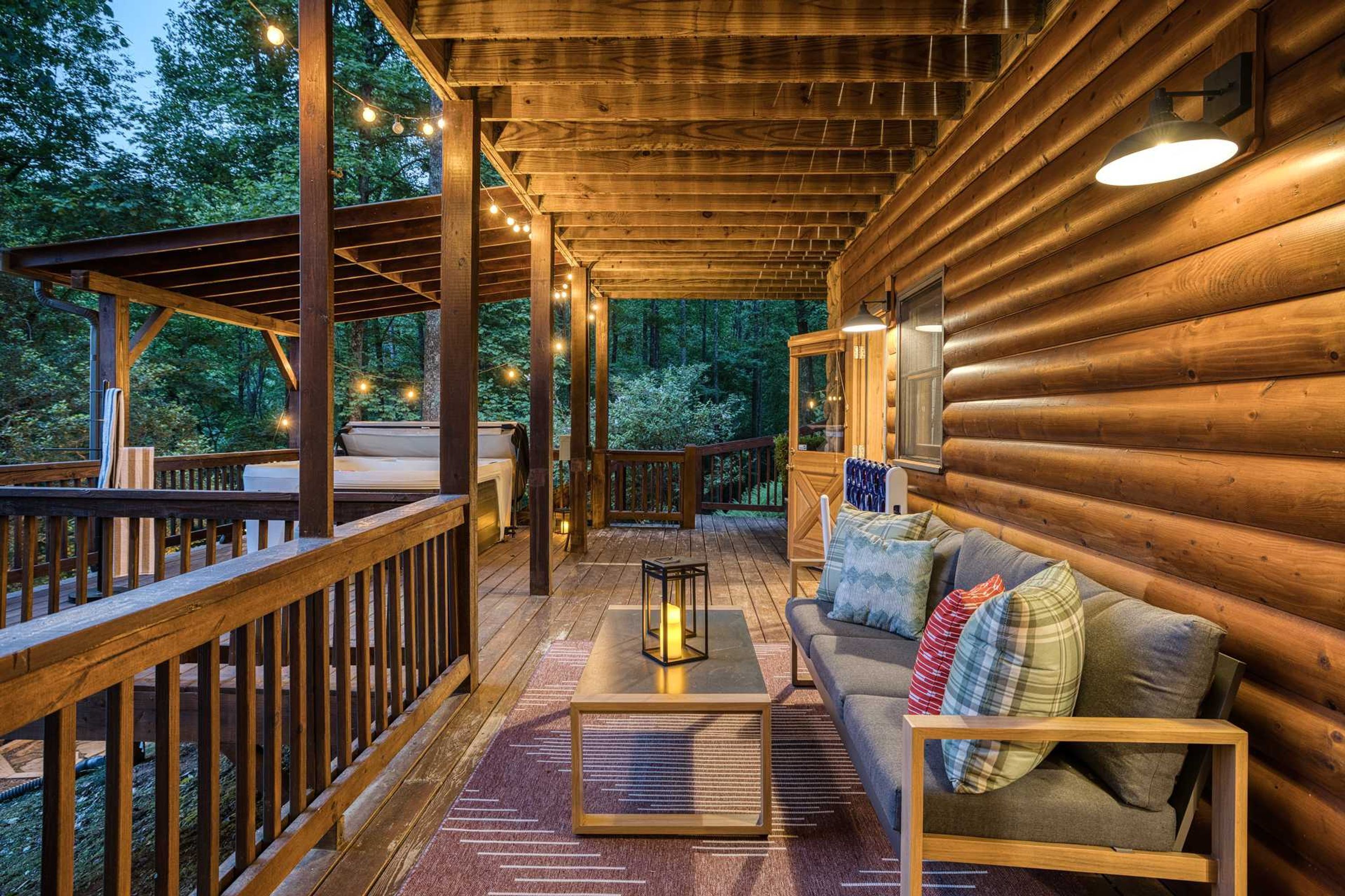 A wooden cabin with a deck, a sofa with cushions, a table, and string lights.