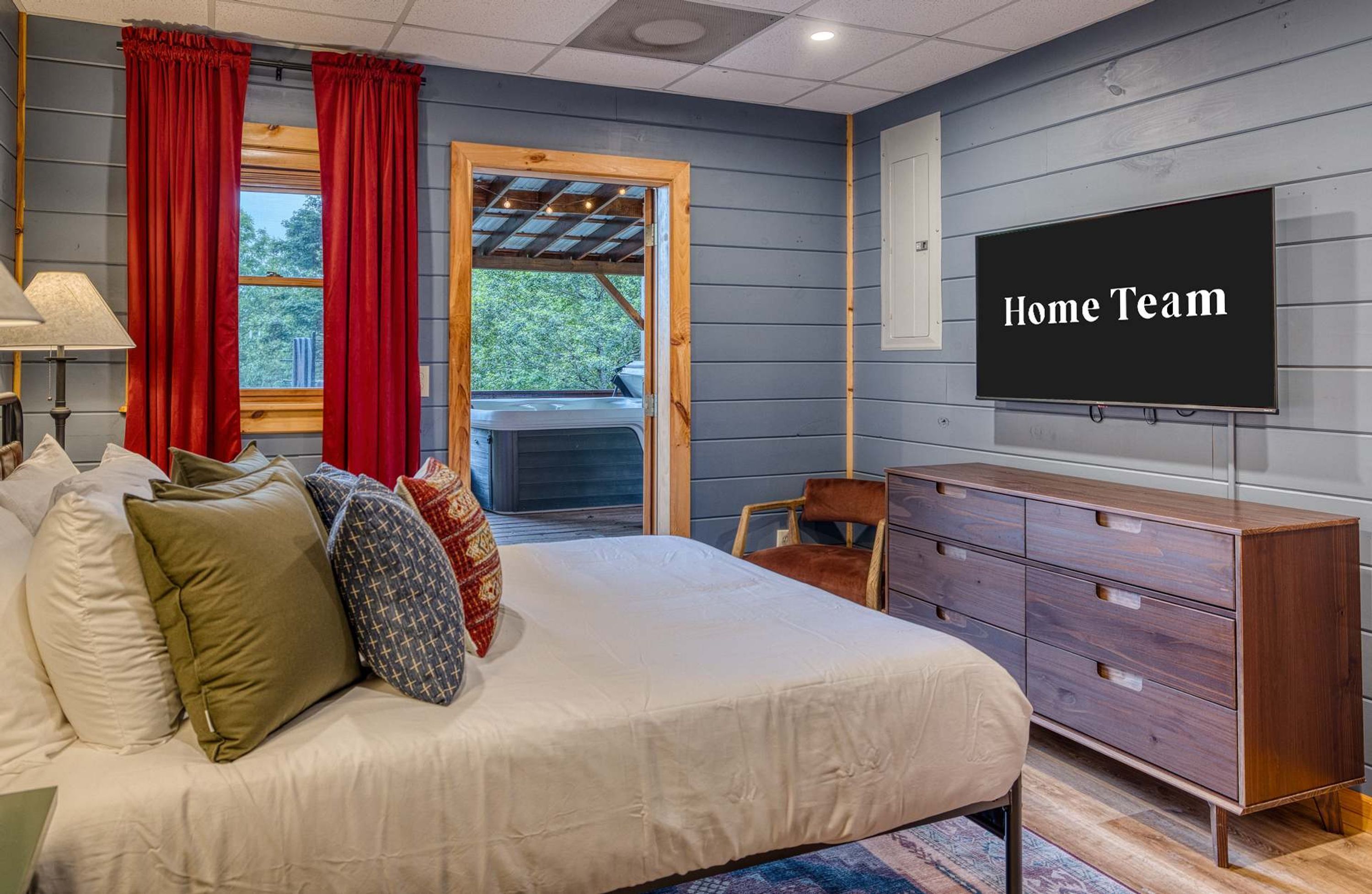 A bedroom with a bed, a dresser, a TV, and a window with curtains.