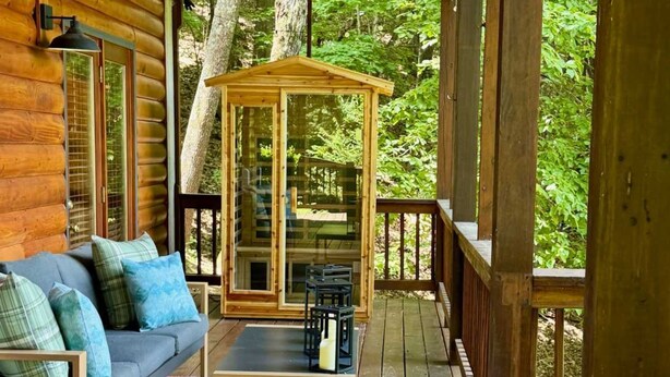 Eine Holzhütte mit Veranda, einer Couch, einem Tisch und einer Glashaube.