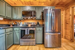 Una cocina moderna con electrodomésticos de acero inoxidable, gabinetes verdes y suelo de madera.