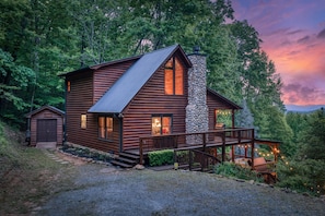 A log cabin with a stone chimney, a porch, and a view of the surrounding forest. - Blue Ridge Treehouse Escape Views Hot Tub (Blue Ridge)