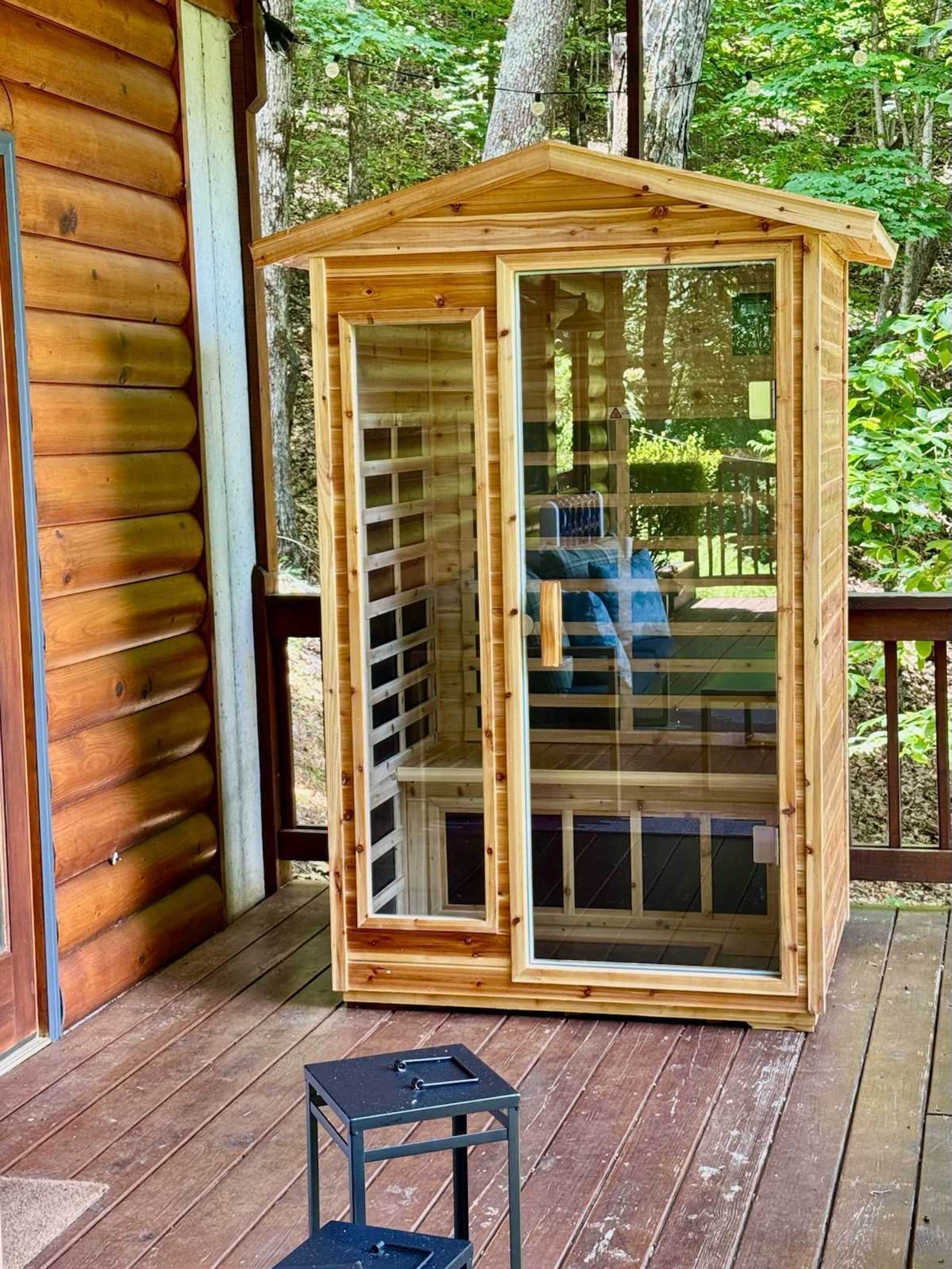Une cabane en bois dotée d’une véranda en verre, d’une terrasse et d’une petite table.