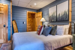A bedroom with a bed, pillows, a nightstand, a lamp, and a painting of a forest on the wall. - Blue Ridge Treehouse Escape Views Hot Tub (Blue Ridge)