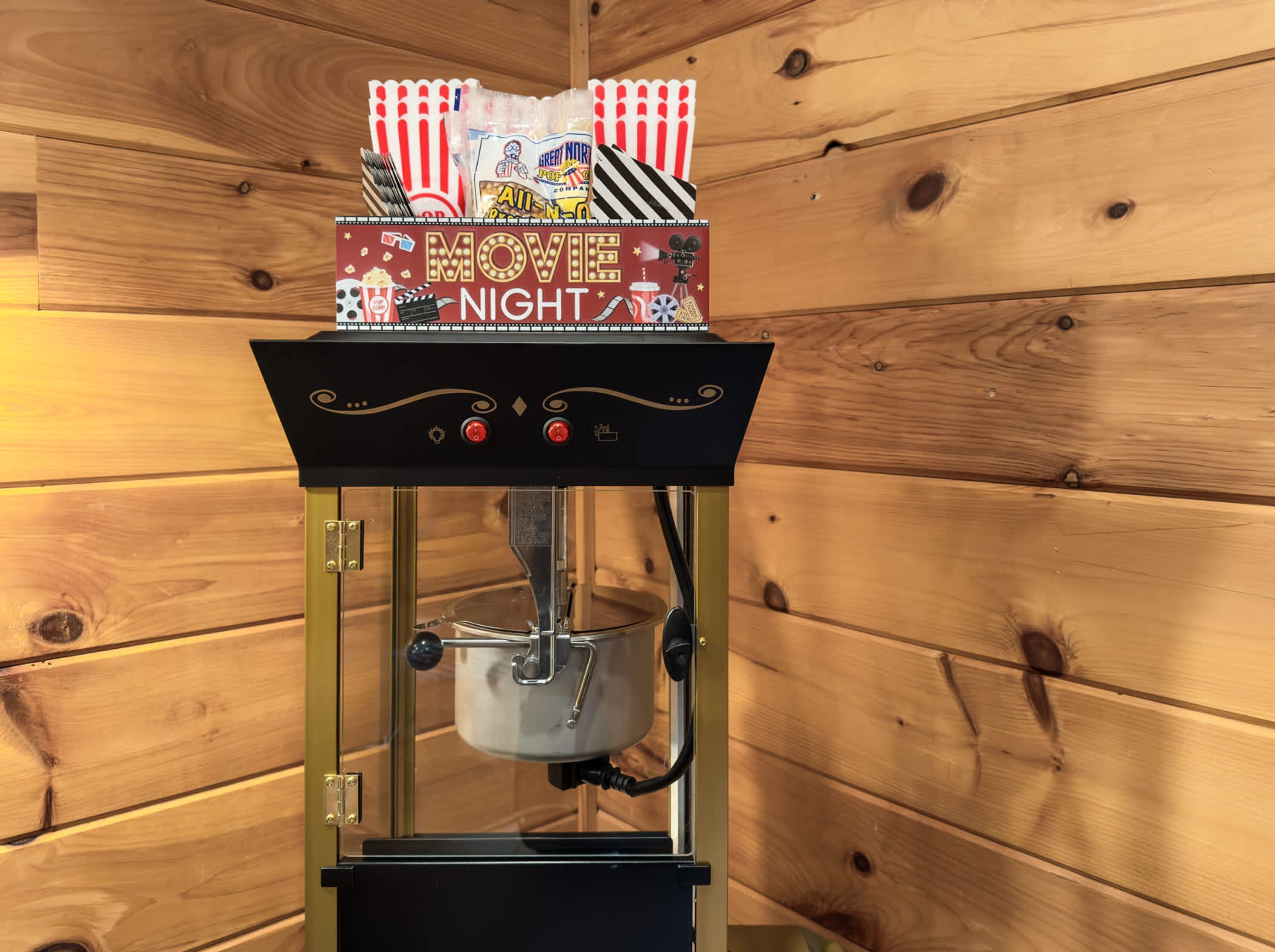 Een popcornmachine met een 'MOVIE NIGHT' bordje erboven, voor een houten wand.