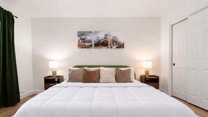 A bedroom with a large bed, two bedside tables with lamps, a green headboard, and a door on the right. - Sleeps 16 Heated Pool Arcade Backyard Resort (Mesa)