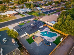 Eine Vogelperspektive auf ein Wohngebiet mit einem Haus, das einen Swimmingpool, Solaranlagen und Sitzgelegenheiten im Freien zeigt.