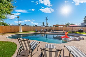 Ein Garten mit Swimmingpool, Liegestühlen und Grillplatz.