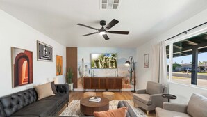 A modern living room with a ceiling fan, a large window, and a view of the outdoors. - Sleeps 16 Heated Pool Arcade Backyard Resort (Mesa)