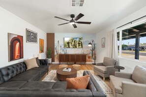 Ein modernes Wohnzimmer mit Deckenventilator, einem großen Fenster und Blick ins Freie.