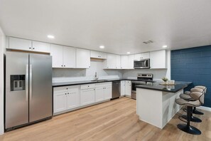 A modern kitchen with white cabinetry, stainless steel appliances, and a wooden floor. - Sleeps 16 Heated Pool Arcade Backyard Resort (Mesa)