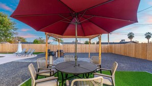 A covered outdoor seating area with a round table and chairs, surrounded by a wooden fence. - Sleeps 16 Heated Pool Arcade Backyard Resort (Mesa)