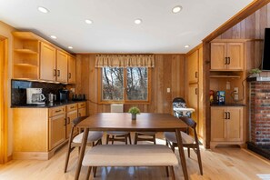 A kitchen with wooden cabinets, a dining table, and a window with a view of trees. - 4 Br Mtn Cabin Sauna Hot Tub Fire Pit Putt Putt (Albrightsville)