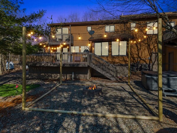 A wooden deck with string lights, a fire pit, and a hot tub. - 4 Br Mtn Cabin Sauna Hot Tub Fire Pit Putt Putt (Albrightsville)