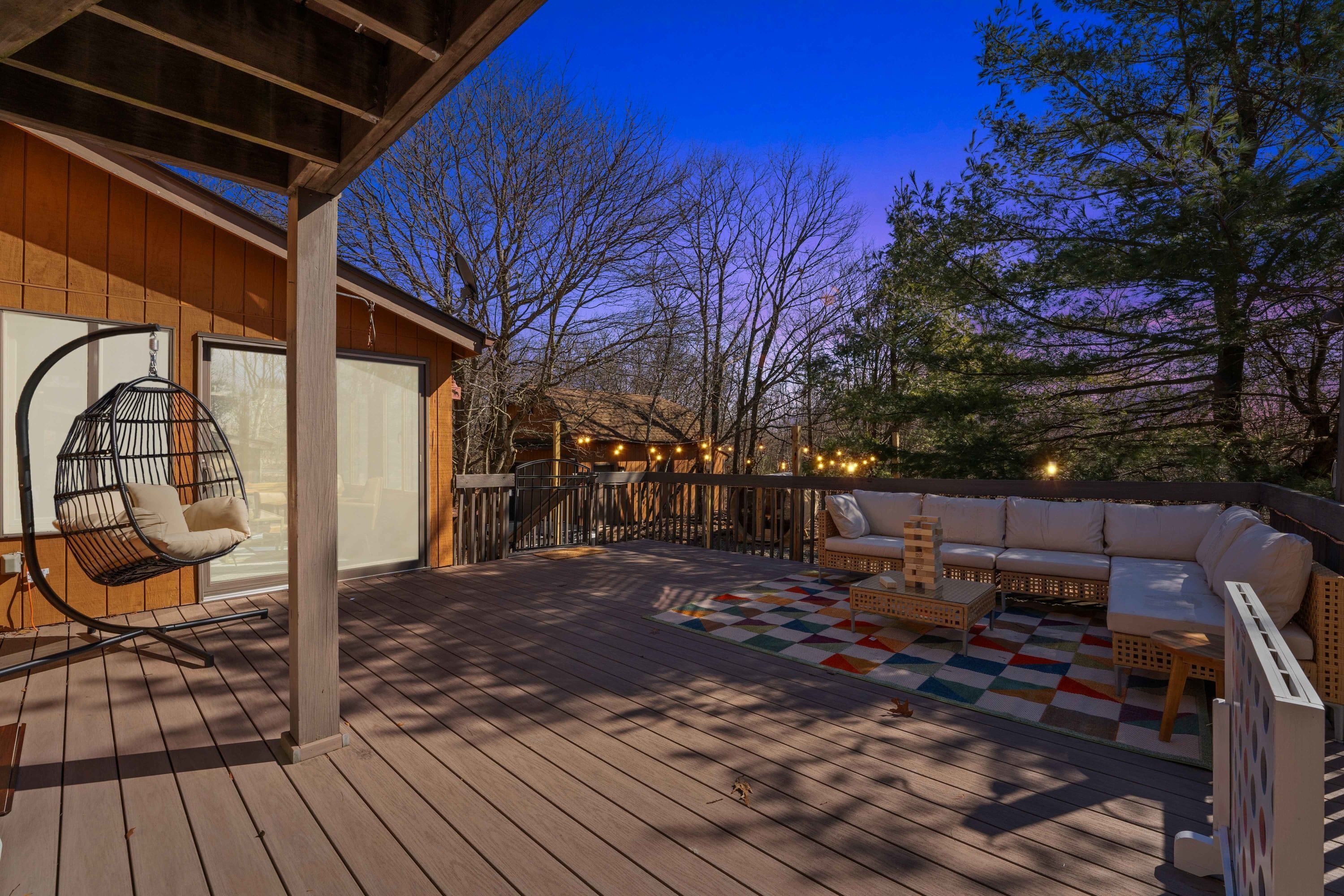 A wooden deck with a hanging chair, a sofa, and a checkered rug.