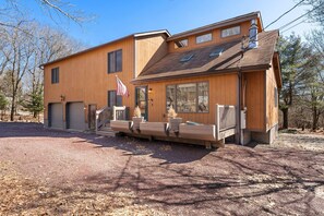 A two-story wooden house with a front porch, a flag, and a garage. - 4 Br Mtn Cabin Sauna Hot Tub Fire Pit Putt Putt (Albrightsville)