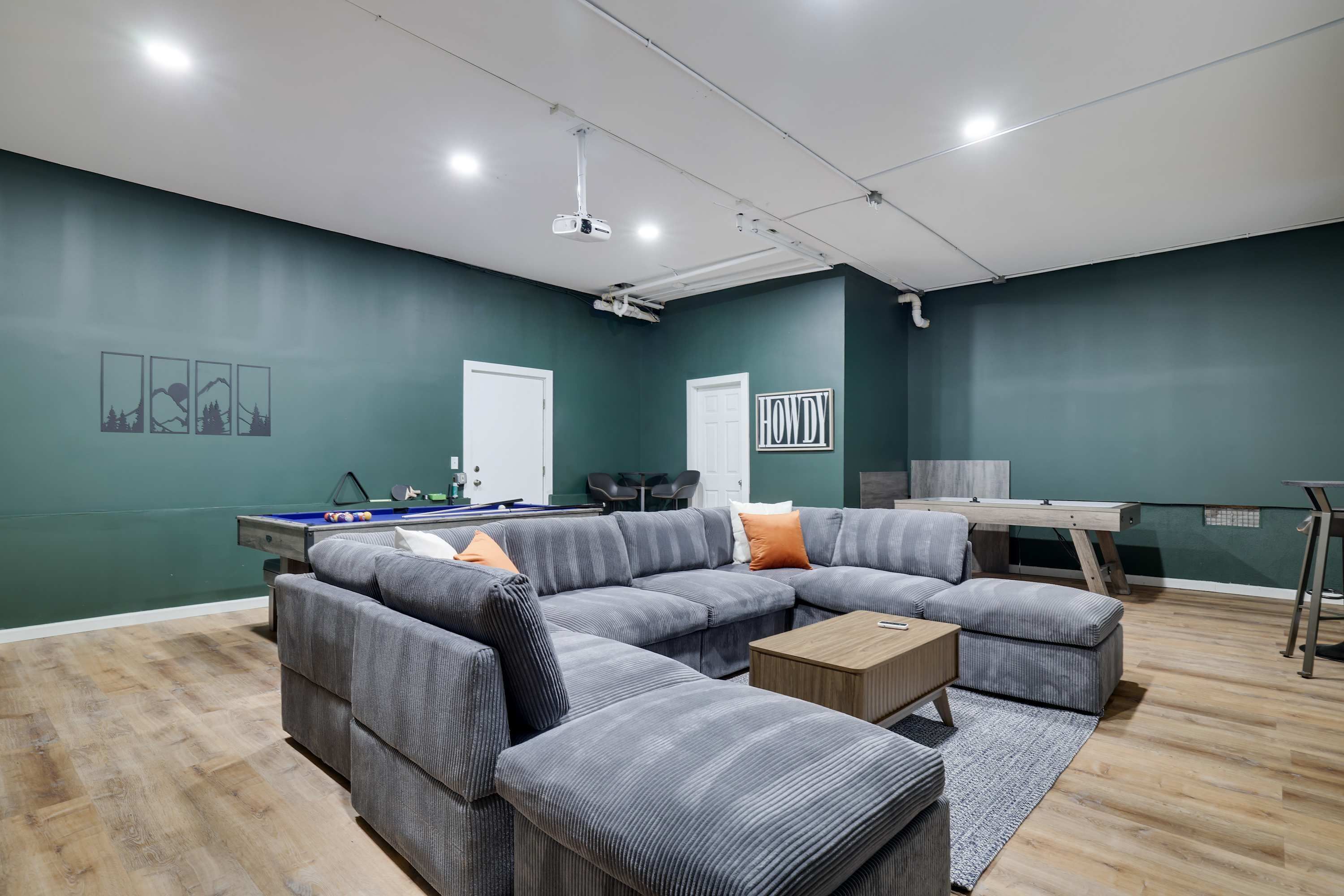 A modern living room with a sectional sofa, a pool table, and a desk.