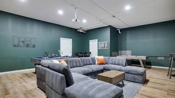 A modern living room with a sectional sofa, a pool table, and a desk.