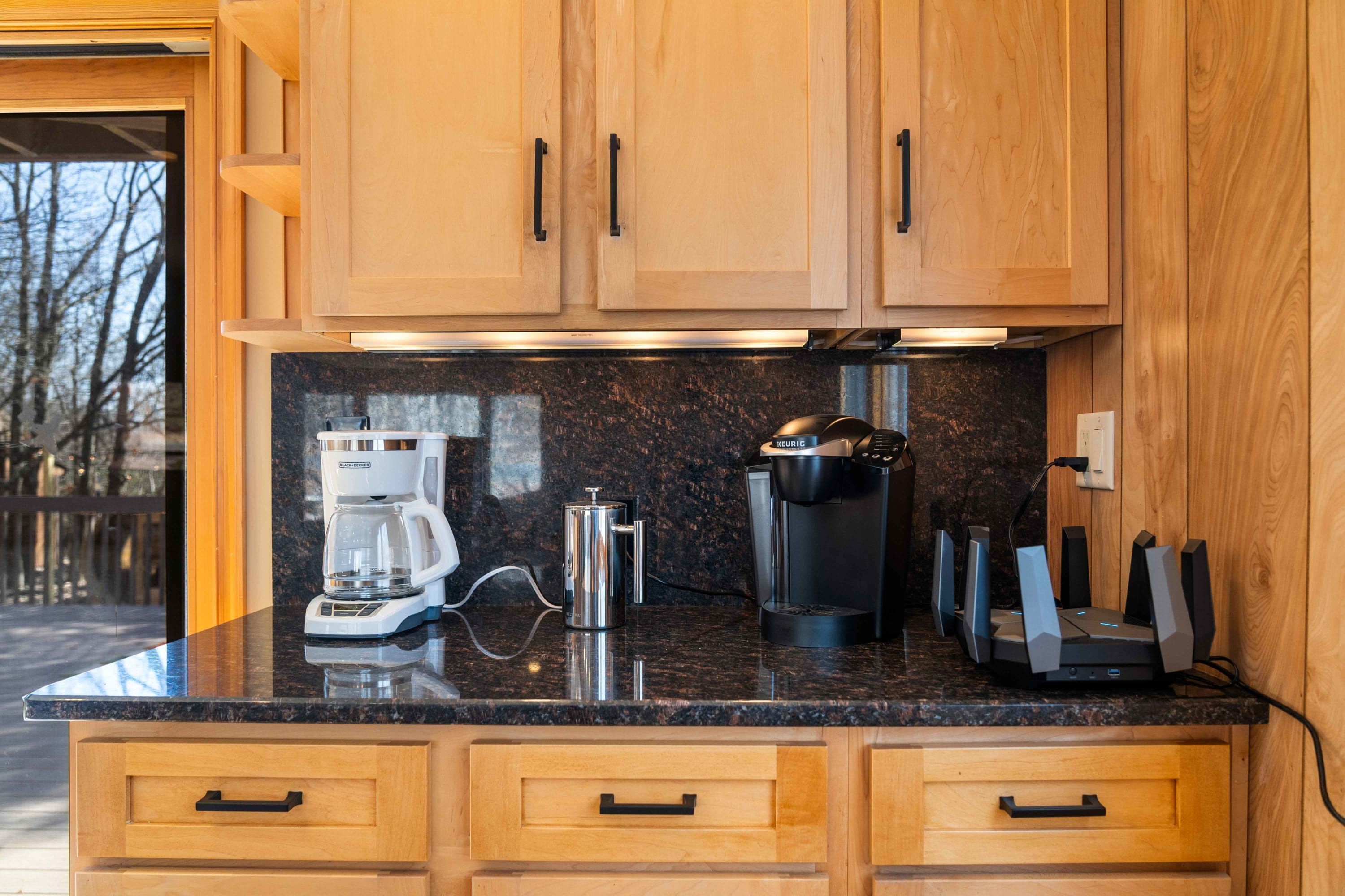 A kitchen with wooden cabinets, a black countertop, a coffee maker, a kettle, and a set of knives.