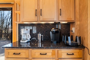 A kitchen with wooden cabinets, a black countertop, a coffee maker, a kettle, and a set of knives. - 4 Br Mtn Cabin Sauna Hot Tub Fire Pit Putt Putt (Albrightsville)