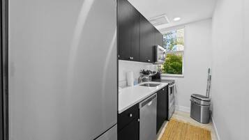 A modern kitchen with black cabinets, a stainless steel refrigerator, and a window with blinds.