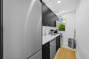 A modern kitchen with black cabinets, a stainless steel refrigerator, and a window with blinds. - Pineapple Paradise 1 13 min to Beach Fire Pit (Sarasota)