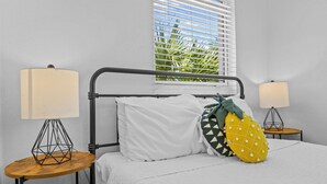 A bed with white bedding, two bedside tables with lamps, a window with blinds, and a pineapple-shaped pillow. - Pineapple Paradise 1 13 min to Beach Fire Pit (Sarasota)