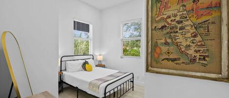 A bedroom with a bed, a nightstand, a lamp, and a map of Florida on the wall.