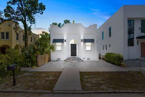 Una casa moderna de dos pisos con fachada blanca, puerta principal negra y un pequeño porche.