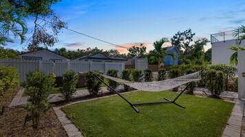 A backyard with a hammock, a lawn, a white fence, and houses in the background.