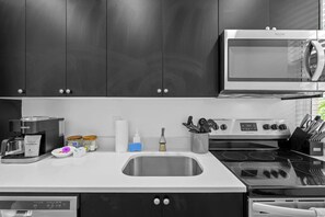 Una cocina moderna con armarios oscuros, microondas integrado, cafetera y pileta de acero inoxidable.