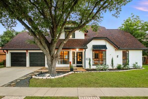 Une maison à deux étages avec un garage, un grand arbre à l’avant et une pelouse bien entretenue.