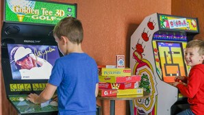 Two children playing a golf video game with a scoreboard and various game boxes on a table. - Pool Games Pickleball Putt Putt Fun (San Antonio)