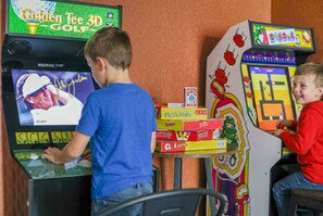 Zwei Kinder spielen ein Golf-Videospiel mit einer Anzeigetafel und verschiedenen Spielstationen auf einem Tisch.