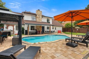 Ein Garten mit Swimmingpool, Gartenmöbeln und Grillplatz.