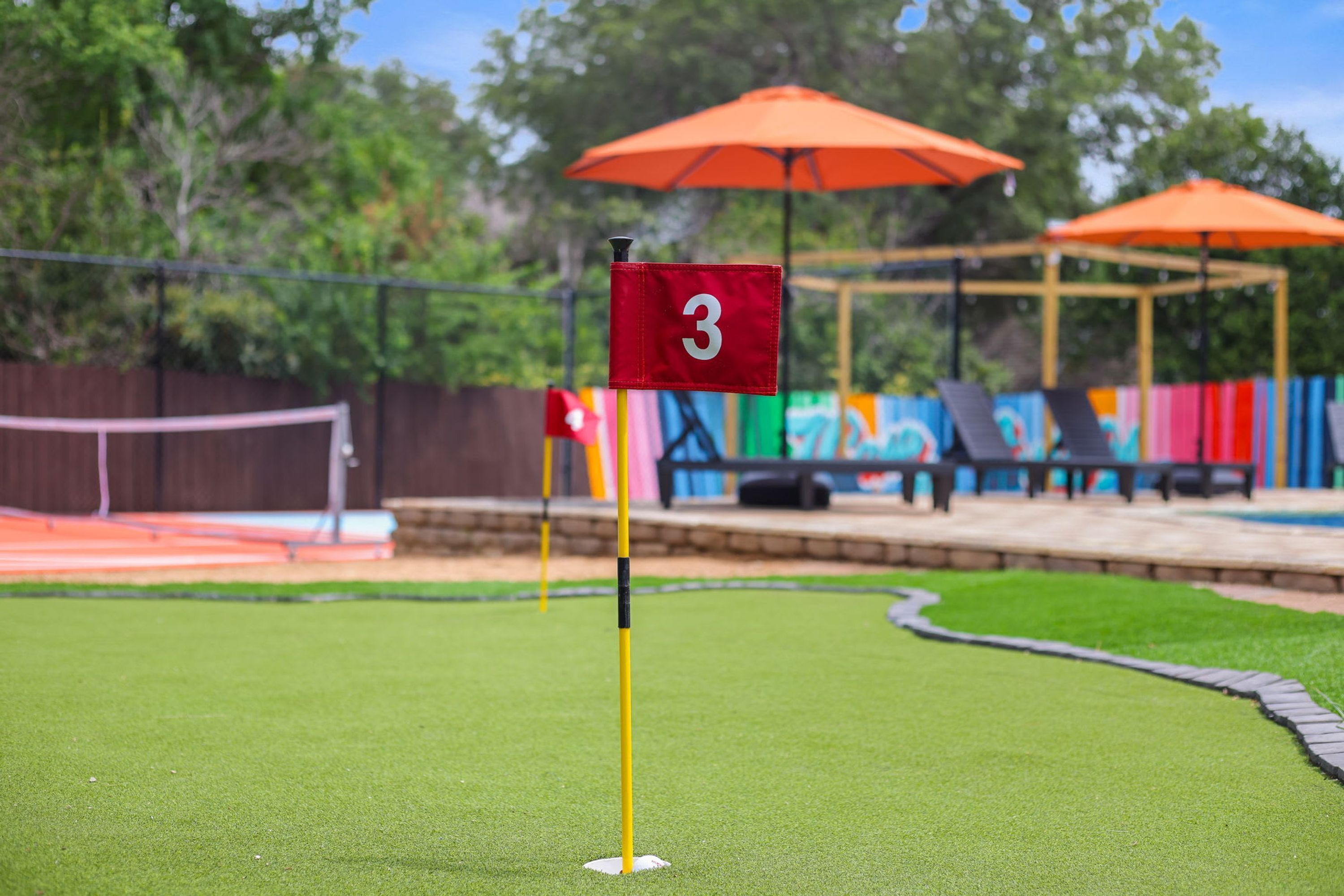 A miniature golf course with a red flag marked '3' on a yellow pole, surrounded by artificial grass.