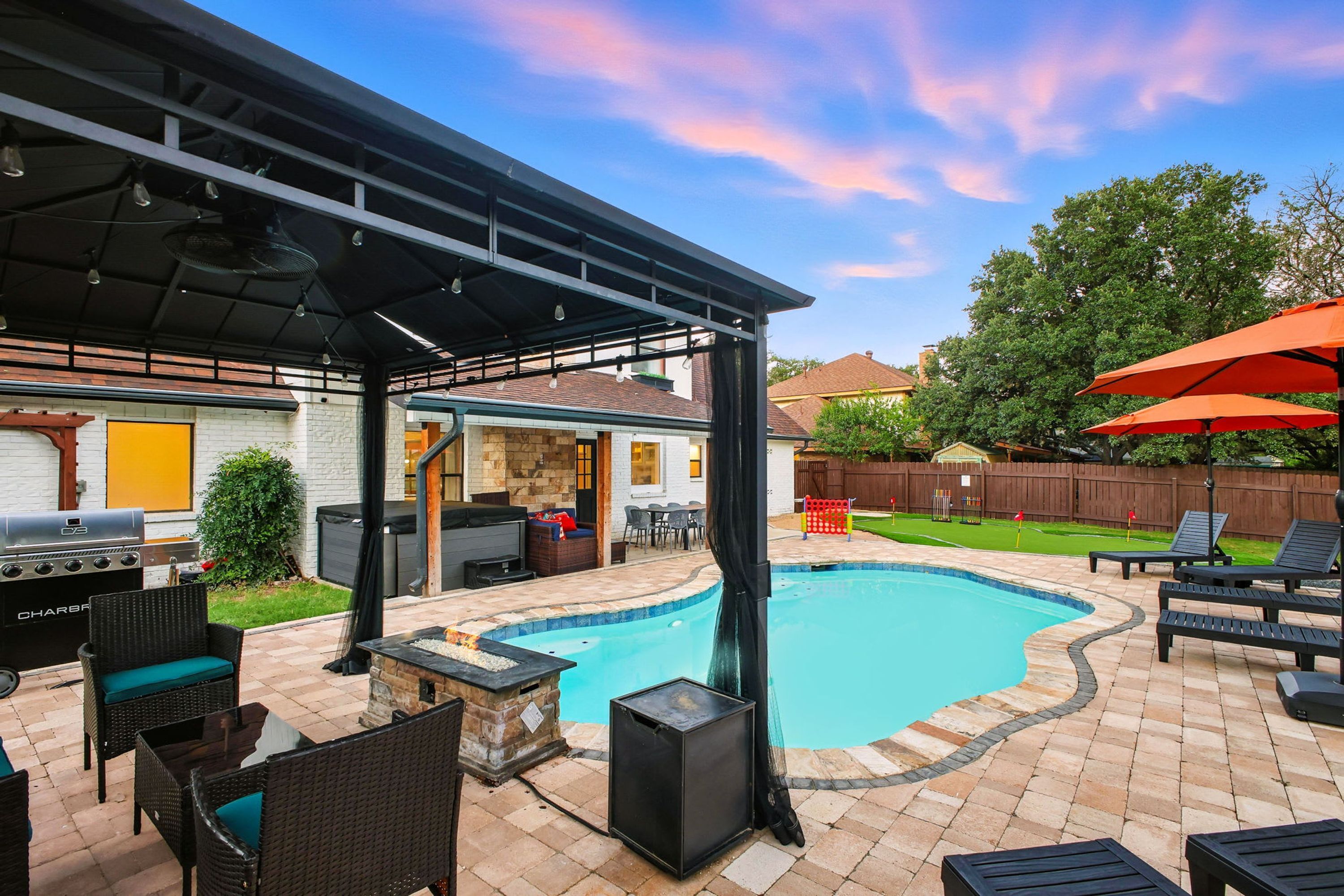Ein Garten mit Schwimmbad, Gartenmöbeln, Grill und überdachter Terrasse.