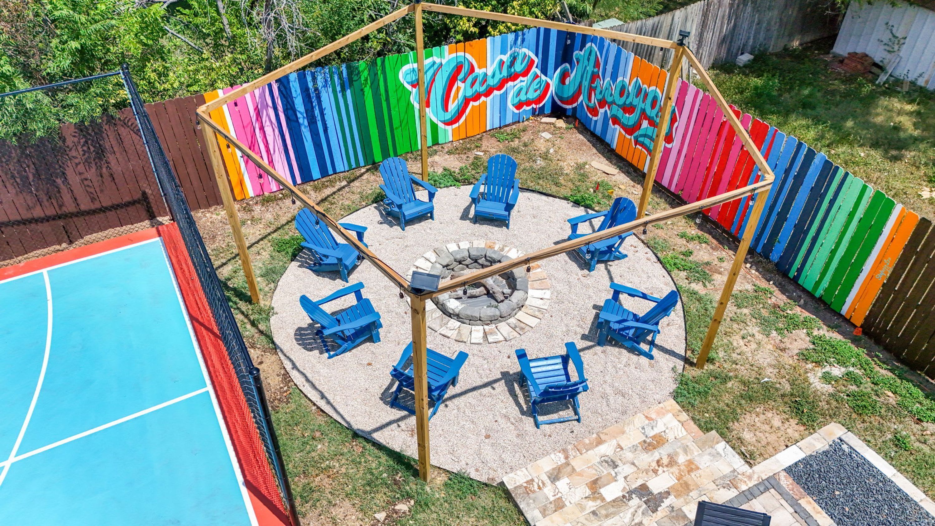 A circular outdoor seating area with blue chairs and a fire pit, surrounded by a colorful fence with a mural.