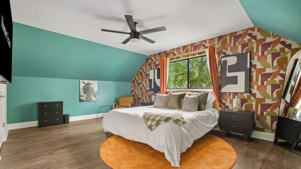 A bedroom with a bed, a ceiling fan, a window with curtains, and a patterned wall. - Pool Games Pickleball Putt Putt Fun (San Antonio)