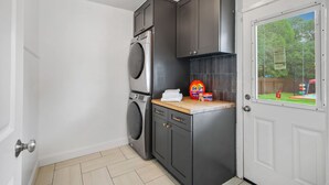 A compact laundry room with a washing machine, dryer, and a small countertop with a bottle of Tide detergent and a box of Bounce fabric softener. - Pool Games Pickleball Putt Putt Fun (San Antonio)